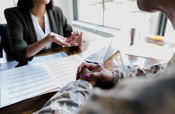 Female financial advisor gestures during meeting with unrecognizable female army veteran.